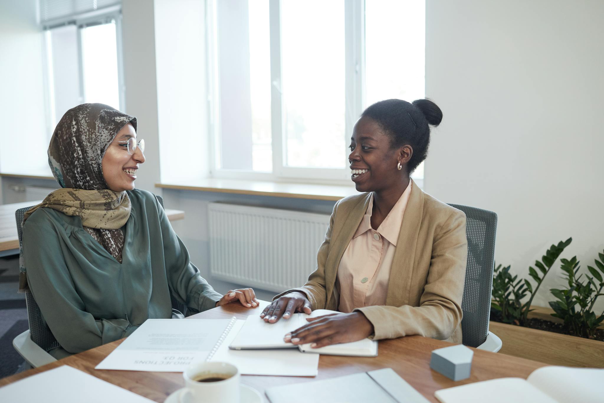 Two diverse women in a business meeting, discussing documents in an office setting.